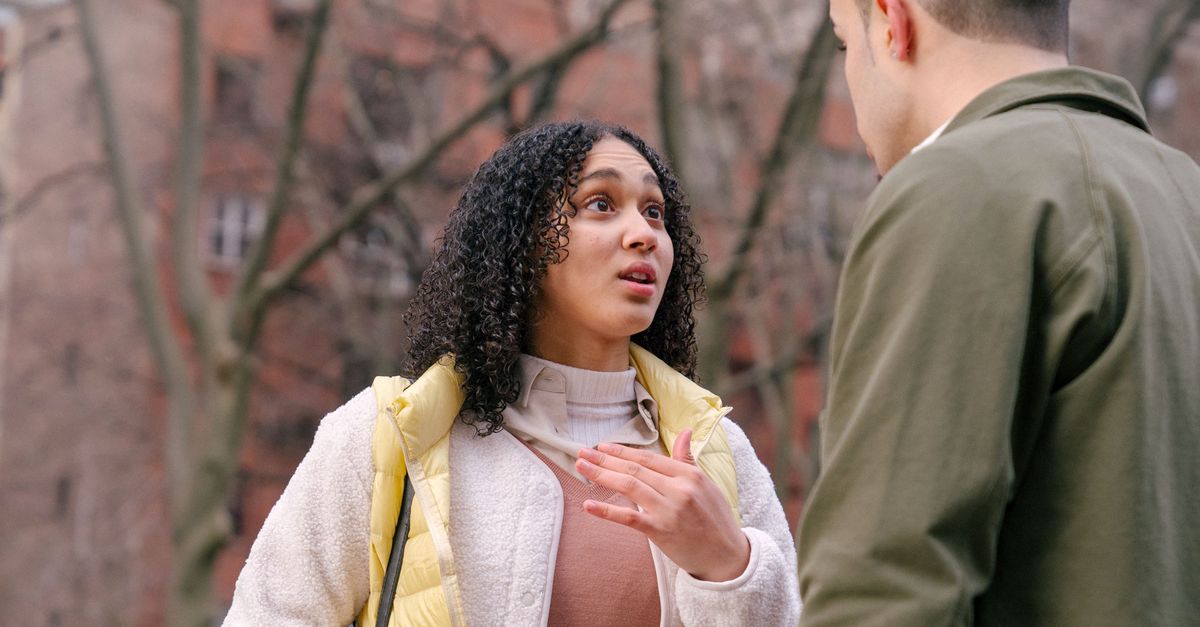 From below of ethnic female with short curly hair standing and arguing with boyfriend on street in daylight