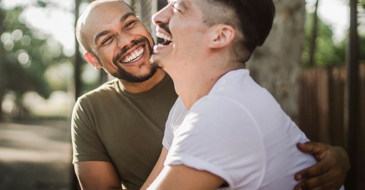 Happy interracial gay couple laughing and embracing outdoors, showcasing love and happiness.