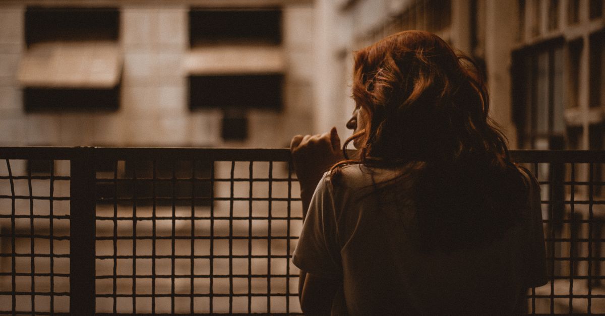 A woman stands alone looking through a railing with a sepia-toned, contemplative mood.