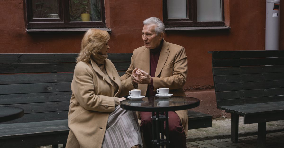 An elderly couple enjoys a conversation over coffee at an outdoor cafe.