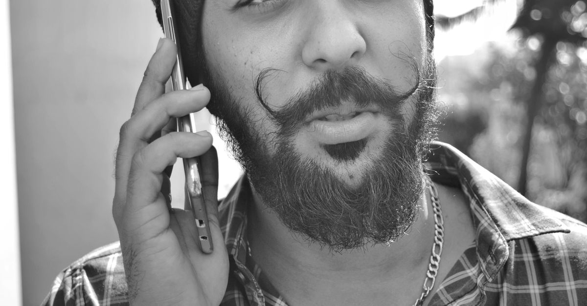 Black and white close-up of a bearded man using a smartphone outdoors.