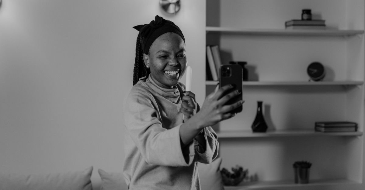 A happy woman takes a selfie indoors, capturing a joyful moment in grayscale.