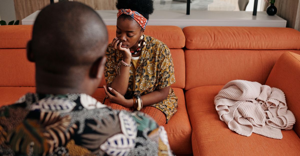 A thoughtful couple engaged in a deep discussion on a vibrant orange sofa in a modern living room.
