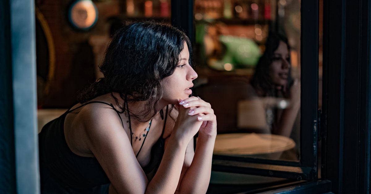 A thoughtful woman in a cozy cafe looks outside, reflecting on a peaceful day.