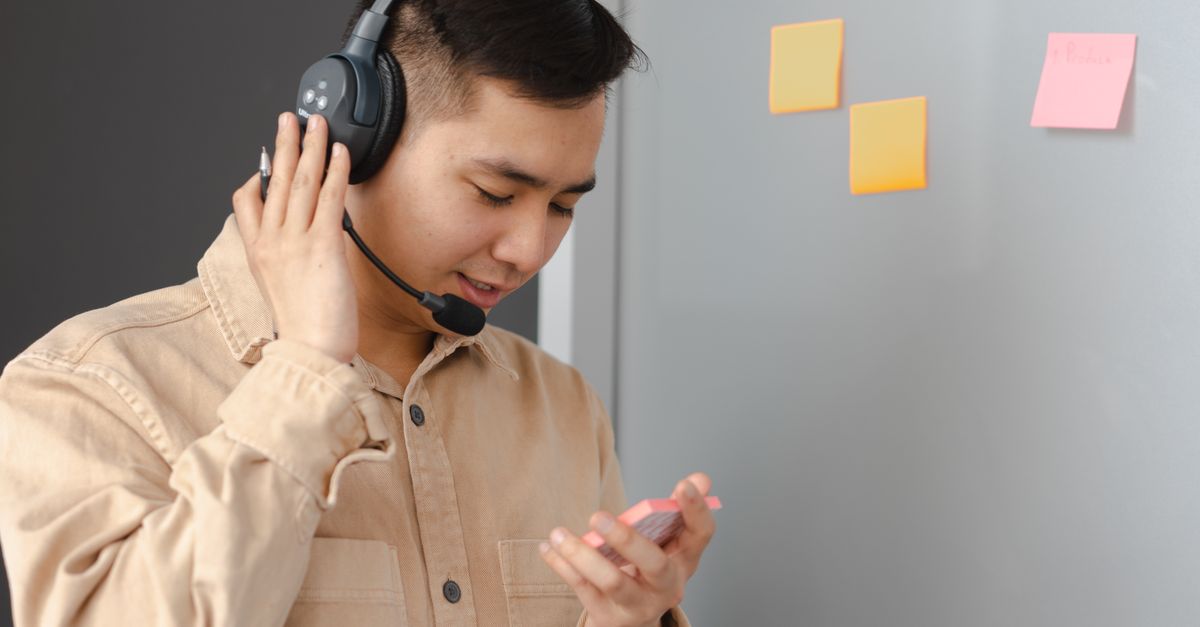 Asian man wearing headset, consulting with clients, holding notes in front of sticky notes.