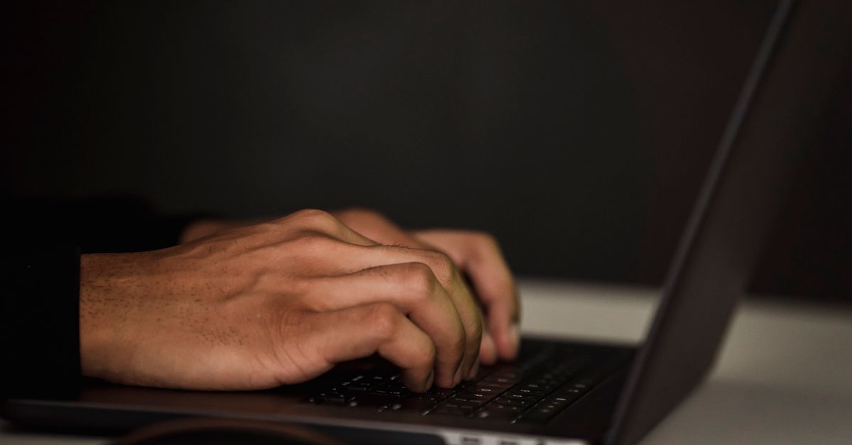 Crop unrecognizable person surfing internet on contemporary netbook and typing on keyboard in dark workspace